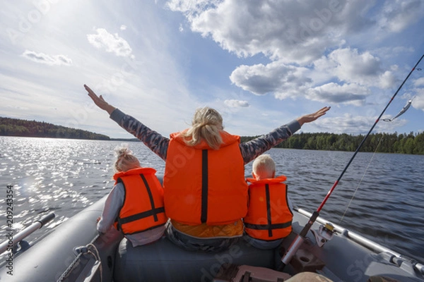 Fototapeta Girl in a life jacket floating on the boat with his hands up. Children in life jackets sitting next