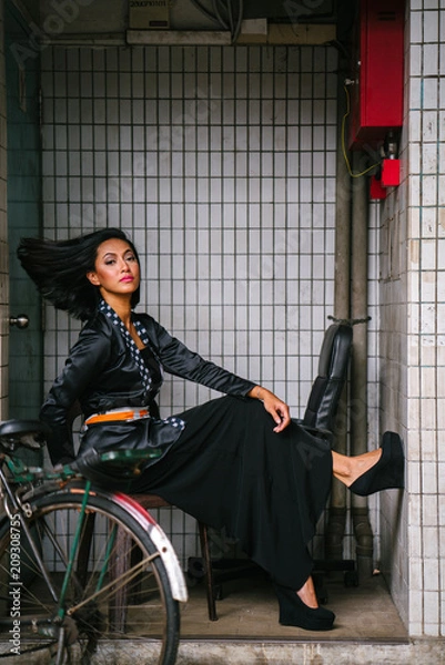 Fototapeta Fashion portrait of a young, slim, attractive and fashionable Muslim Malay woman sitting and posing on a chair in a city in Asia. 