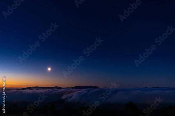 Fototapeta Quarto di Luna nel cielo sereno all’alba sopra una distesa di nuvole bianche