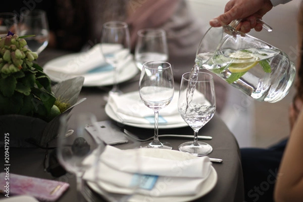Fototapeta The waiter pours water with lemon and mint into glasses on a serving table