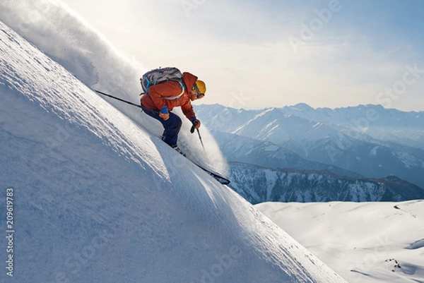 Obraz narciarz jeździ freeride po puchu w dół stoku na tle gór