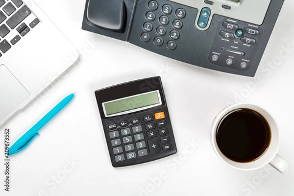 Fototapeta Conceptual workspace or business concept. Laptop computer with cup of coffee, blue pen and modern IP phone and calculator on white background. Top view