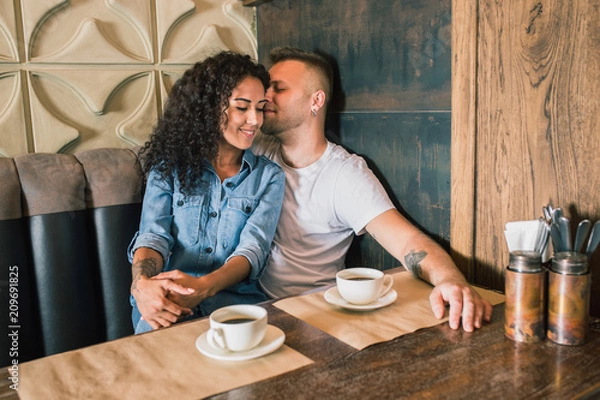 Fototapeta Happy young couple is drinking coffee and smiling while sitting at the cafe