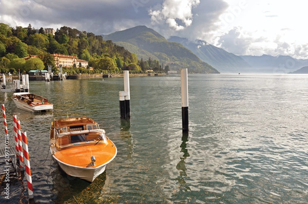 Fototapeta View of Lake Como in a cloudy day with motorboat and harbor in Bellagio, a charming village between the lake and the mountains of Alps. Lombardy region, northern Italy