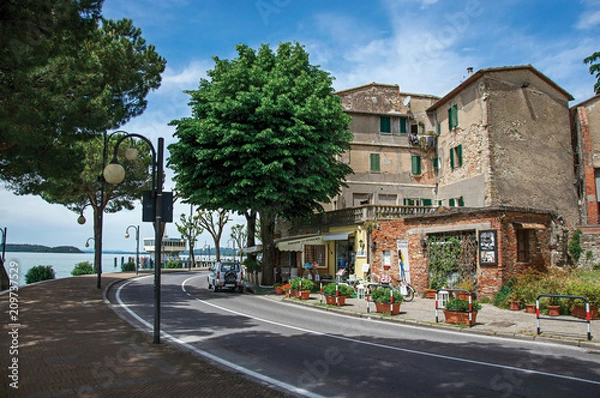 Fototapeta View of the hamlet and its promenade on the shores of Lake Trasimeno, a quiet and picturesque lake near Perugia. Located in Passignano sul Trasimeno, Umbria region, central Italy.