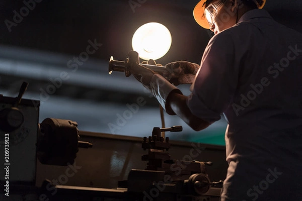 Fototapeta Mechanic Engineer Turner Miller verifies the accuracy of manufacturing steel parts with a scale the size of the measurement device. In the dark room with lamp background.