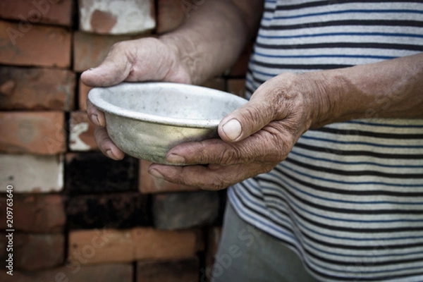 Fototapeta The poor old man's hands hold an empty bowl. The concept of hunger or poverty. Selective focus. Poverty in retirement.Homeless. Alms