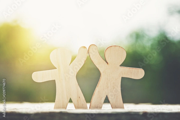 Fototapeta Wooden little men holding hands on natural sunlight background. Symbol of friendship, love and teamwork
