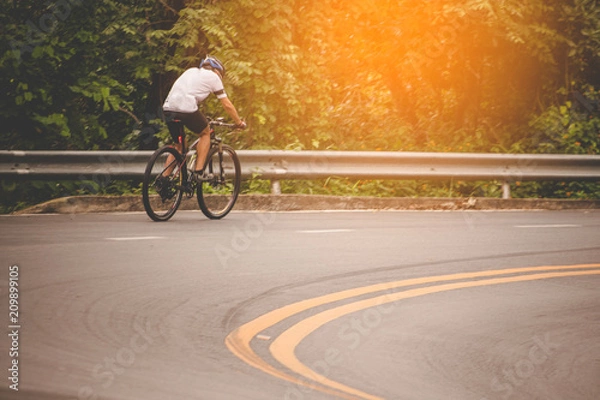 Fototapeta Cyclist in the park with orange sunlight scattered throughout