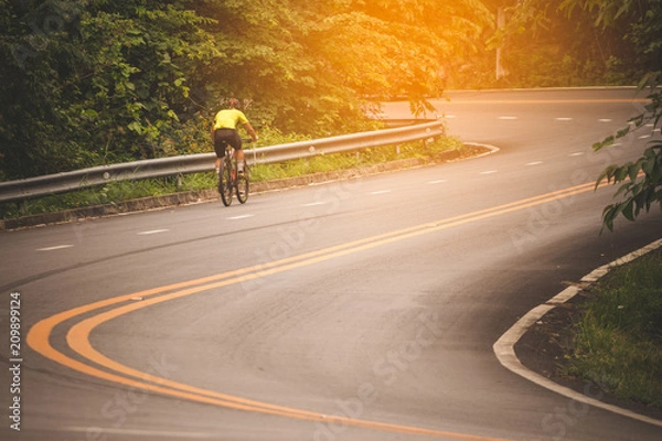 Fototapeta Cyclist in the park with orange sunlight scattered throughout