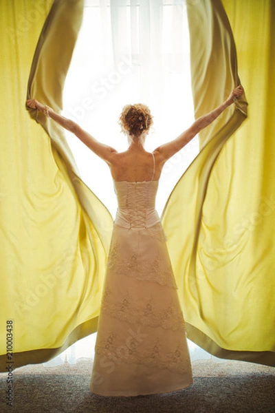 Fototapeta Bride opens beige curtains standing before bright window