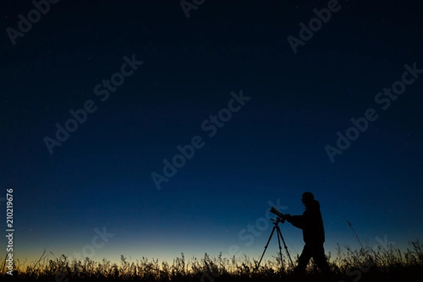 Obraz Astronom fotografuje nocne rozgwieżdżone niebo aparatem cyfrowym za pomocą statywu.