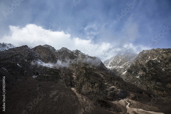 Obraz Горный пейзаж. Вершины в белых облаках, Красивый вид на живописное ущелье, панорама с высокими горами. Природа Северного Кавказа, отдых в горах