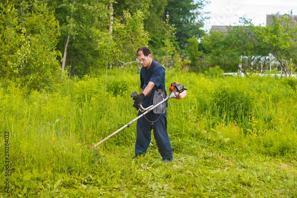 Fototapeta man mowing grass with a lawn mower