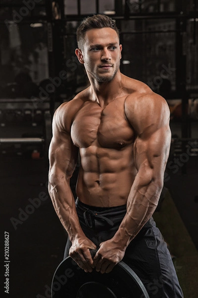 Fototapeta Young handsome sportsman bodybuilder weightlifter with an ideal body, after coaching poses in front of the camera, abdominal muscles, biceps triceps. In sportswear.