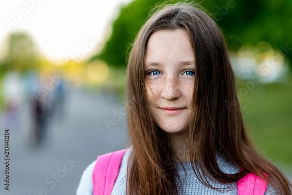 Fototapeta A beautiful child, teenage girl. Summer in nature. Close-up portrait. Blue eyes freckles on face. Smiles happily. Free space for text. Concept of rest. Emotion of pleasure.