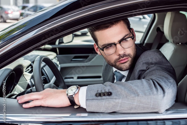 Fototapeta side view of pensive businessman in eyeglasses looking away while driving car