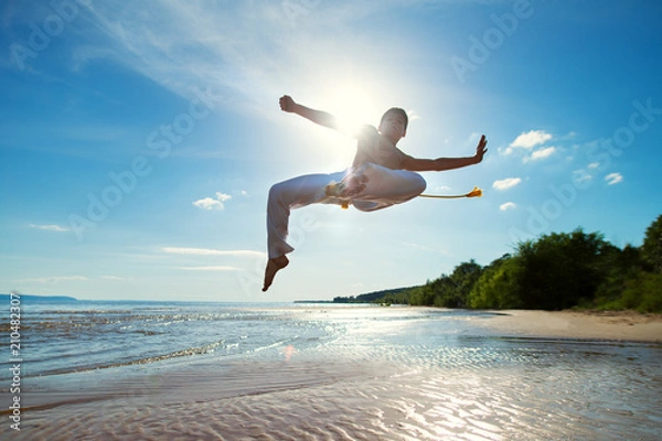 Obraz A young guy trains capoeira on the beach.