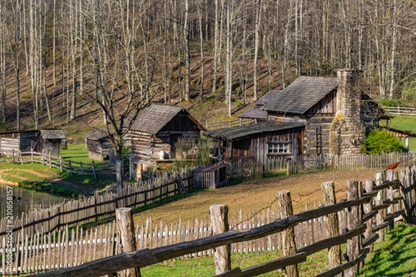 Fototapeta A rustic log cabin farm or homestead with a fence leading the way.