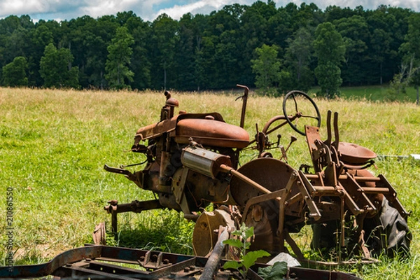 Fototapeta A red, rusty old tractor in a feild of green grass.