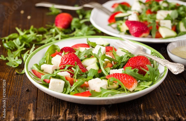 Fototapeta Fresh vegetable strawberry salad on white plate on natural rustic desk.