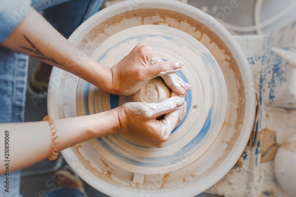 Obraz Widok z góry na ręce z gliny wytwarzającej ceramiczny garnek na kole garncarskim, hobby i wypoczynek z koncepcją przyjemności