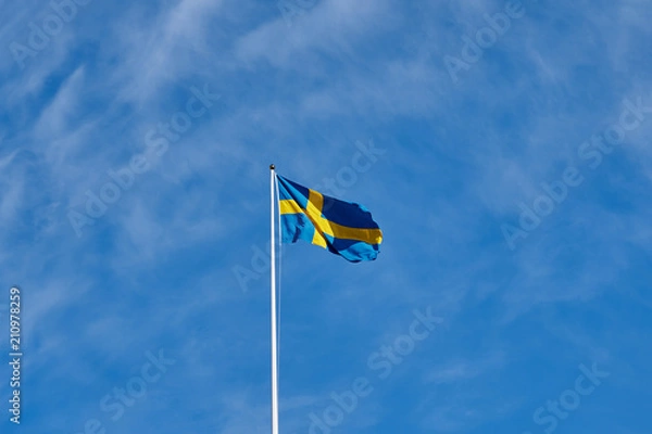 Obraz Flag of Sweden against a blue cloudy sky on a background. 