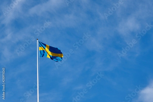 Fototapeta Flag of Sweden against a blue cloudy sky on a background. Copy space for text.