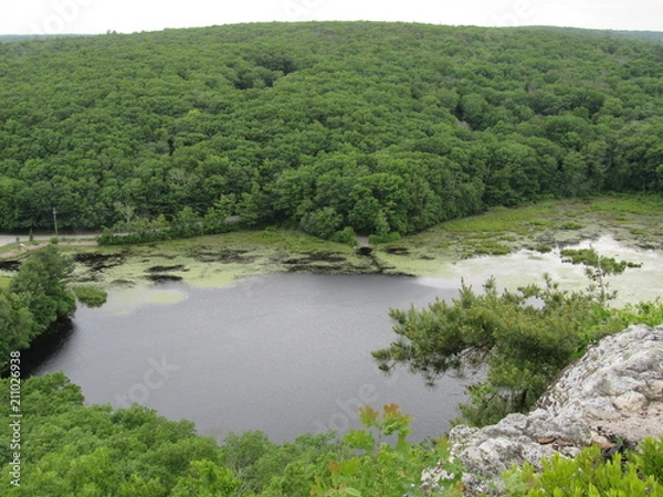 Fototapeta View over the edge of a cliff on a mountain on Lantern Hill trail in Connecticut, with a pond below in the distance 