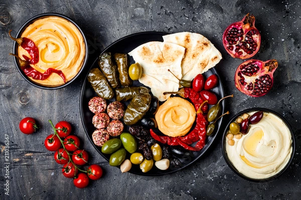 Fototapeta Arabic traditional cuisine. Middle Eastern meze platter with pita, olives, hummus, stuffed dolma, labneh cheese balls in spices. Mediterranean appetizer party idea