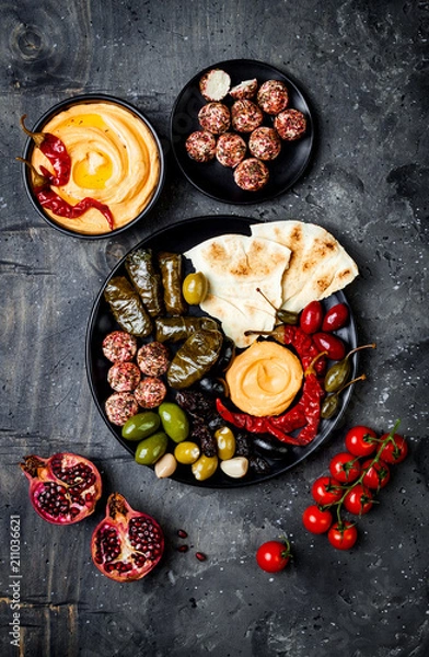 Fototapeta Arabic traditional cuisine. Middle Eastern meze platter with pita, olives, hummus, stuffed dolma, labneh cheese balls in spices. Mediterranean appetizer party idea