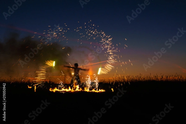 Fototapeta A man with a torch at sunset. Fire show and a lot of the bright sparks in the night