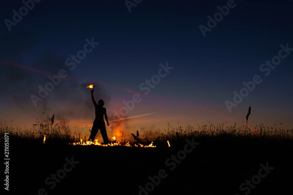 Fototapeta A man with a torch at sunset. Fire show and a lot of the bright sparks in the night