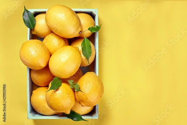 Fototapeta Yellow lemons in a box on a yellow background.  The view from the top. Space for text, copy space