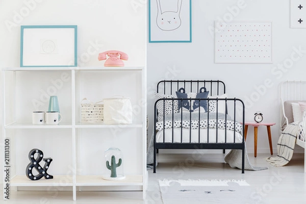 Fototapeta Kid's bedroom interior with a view of one whole bed and a part of the other. Shelves with decorations and posters on the white wall. Real photo