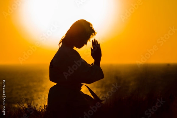 Fototapeta Silhouette of a samurai in a kimono while meditating on the ocean coast, at sunrise. The concept of a healthy lifestyle, unity with nature, meditation.