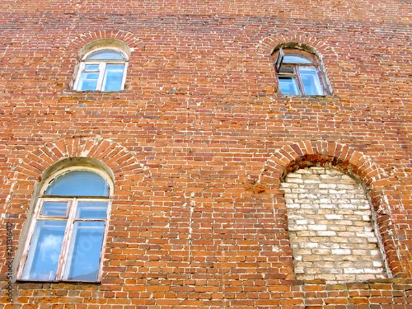 Fototapeta Brick wall of facade of old residential house. Windows have an arched shape. One of the four windows is sealed. On one of the upper floors is open the window leaf.