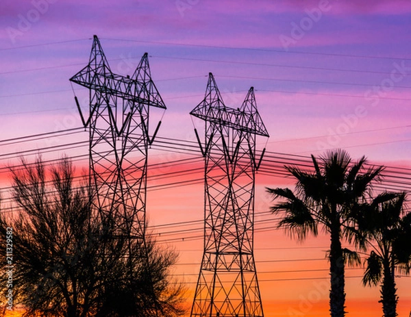 Fototapeta Silhouette of high voltage lines and transmission towers thru the desert at sunset.