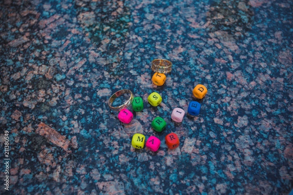 Fototapeta Wooden multicolored letters spelling just married with rings on marble