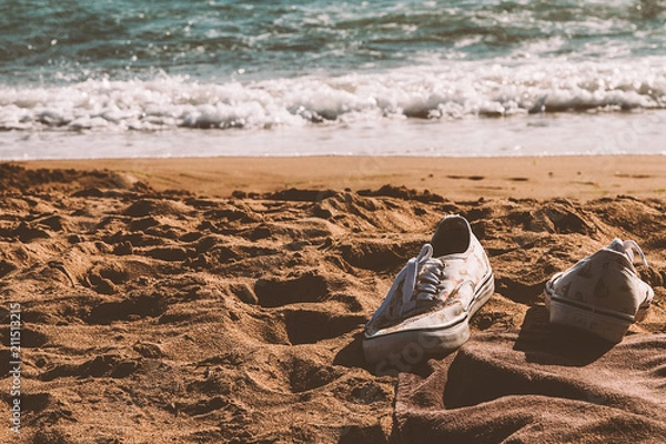 Fototapeta Sneakers left in a sandy beach 