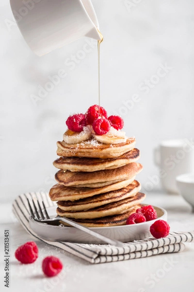 Fototapeta Stack of homemade pancakes with fresh raspberries and poured maple syrup on light concrete background, copy space