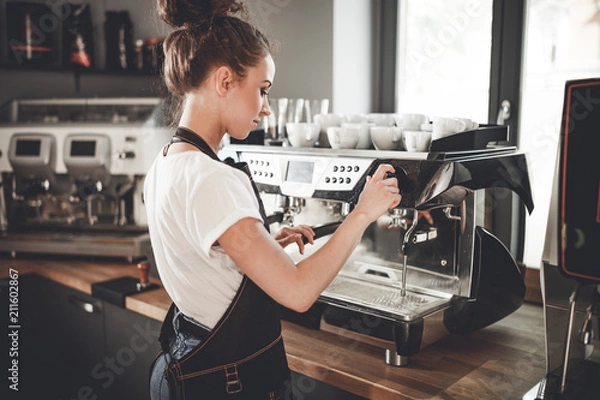 Obraz Młoda kobieta barista przygotowuje kawę za pomocą maszyny w kawiarni