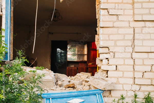 Fototapeta Ruined wall of the house. Hit a military projectile after a car accident. Destruction and earthquake. Migration and crisis. The brick house is destroyed. The window and the wall are broken.