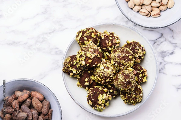 Fototapeta Homemade healthy vegan chocolate avocado truffles with pistachio in the bowl and ingredients on grey marble table. Organic energy vegetarian sweet balls