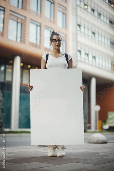Fototapeta Young Intelligent Attractive Woman Holding Blank Canvas Placard Outdoors. Activist Protesting Against Political and Social Issues. Copy Space. Empty Space. Single Person Protest In The City