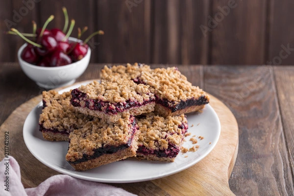 Fototapeta Homemade crumble oatmeal bars with cherries on rustic wooden background, copy space