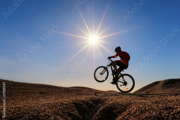 Fototapeta Cyclist riding mountain bike on the rocky trail at sunset.