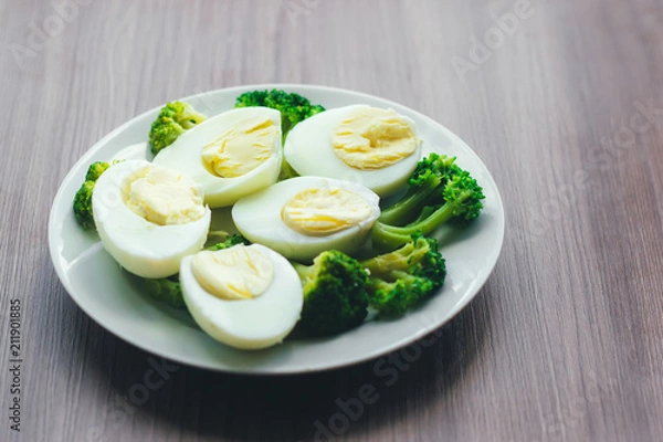 Fototapeta Boiled eggs and broccoli on a white plate on a wooden table.