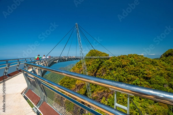 Fototapeta Turyści spacerujący po Langkawi Sky Bridge, zakrzywionym podwieszanym moście dla pieszych, zawieszonym na linach z jednego pylonu, na szczycie Gunung Mat Chinchang na wyspie Langkawi w Kedah w Malezji.