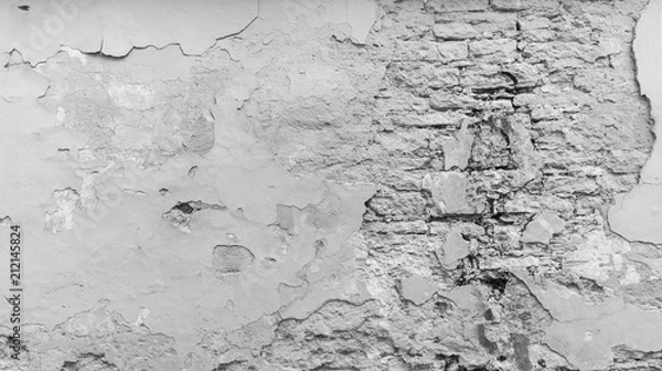 Fototapeta Full frame background of a weathered, damaged and plastered wall painted in black and white. Plaster is partly peeled off revealing old bricks.